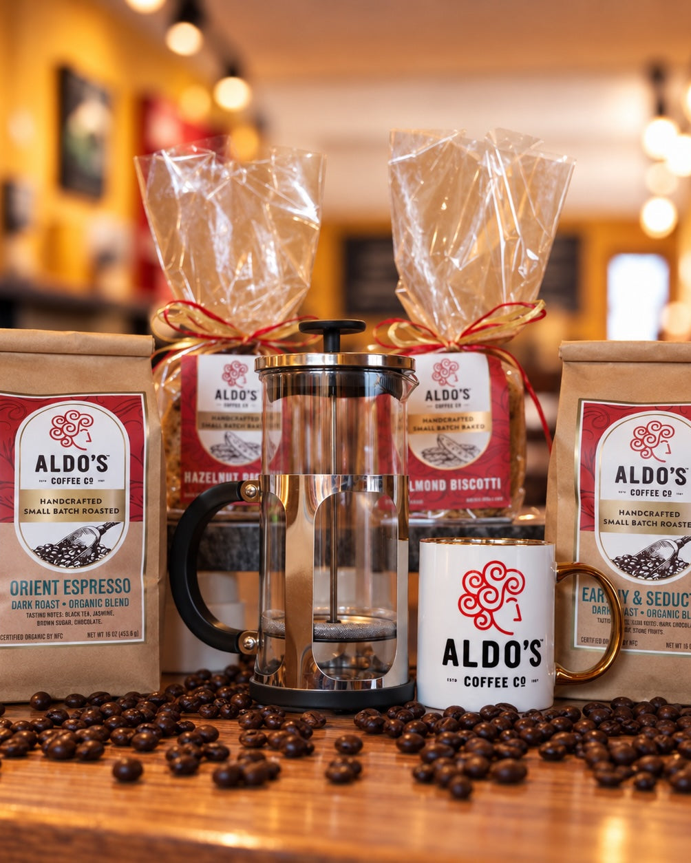 A gift set of coffee and baking items from Aldo's Coffee Co. arranged on a wooden table with scattered coffee beans.