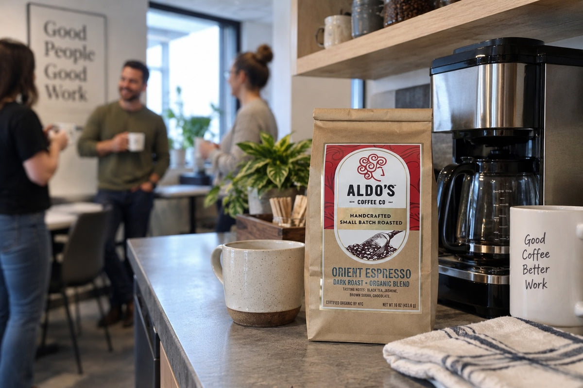 A bag of Aldo's coffee beside an office coffee maker, with coworkers talking in the background